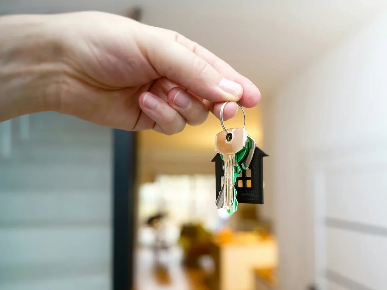 Hand hält einen Schlüsselbund mit Haus-Anhänger vor einer offenen Wohnungstür